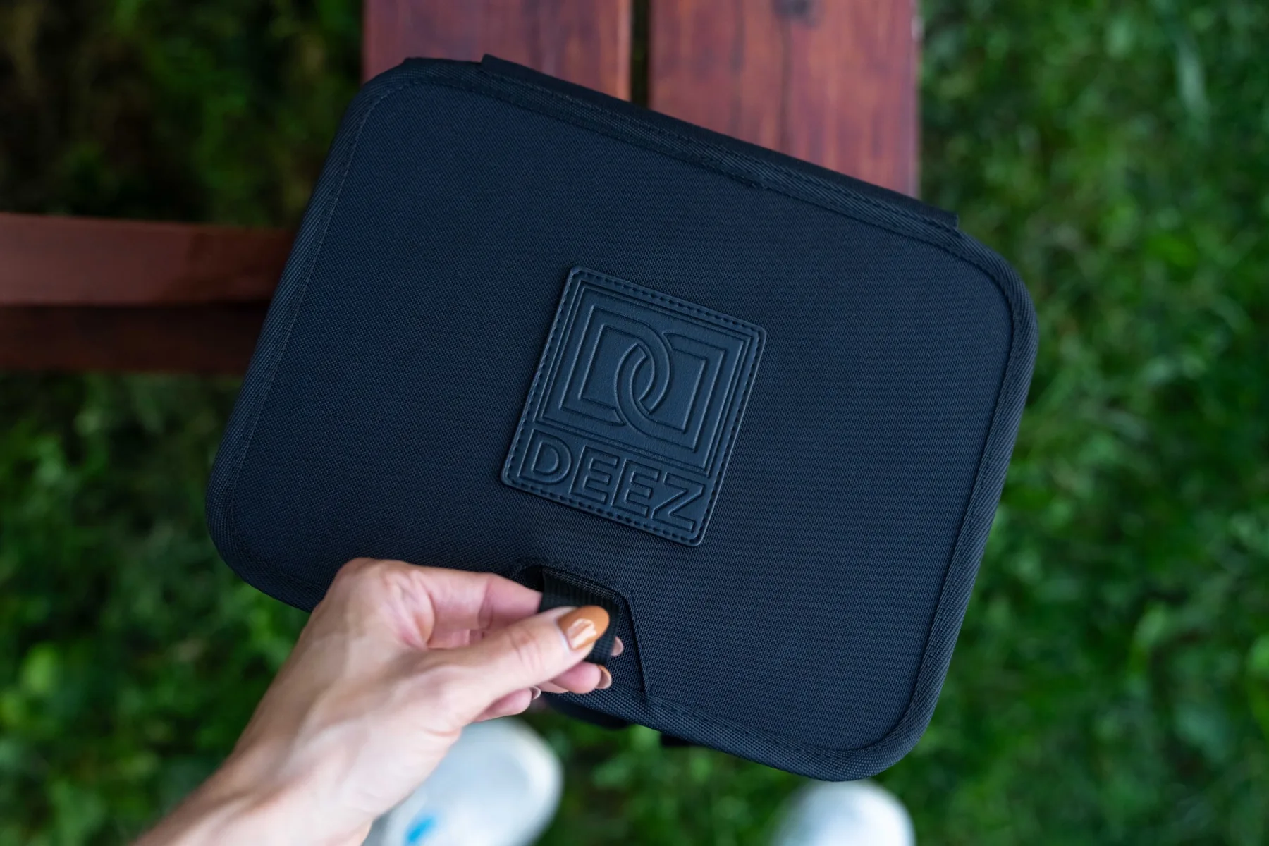 Hand holding the pull tab on the branded black lid of the Double Deez Goodz car trash can.