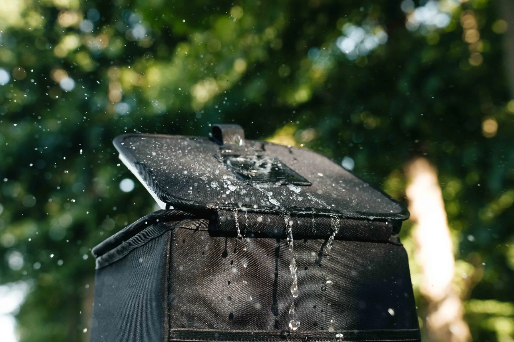 Water splashing over the lid and upper sides of the black Double Deez Goodz car trash can outdoors.