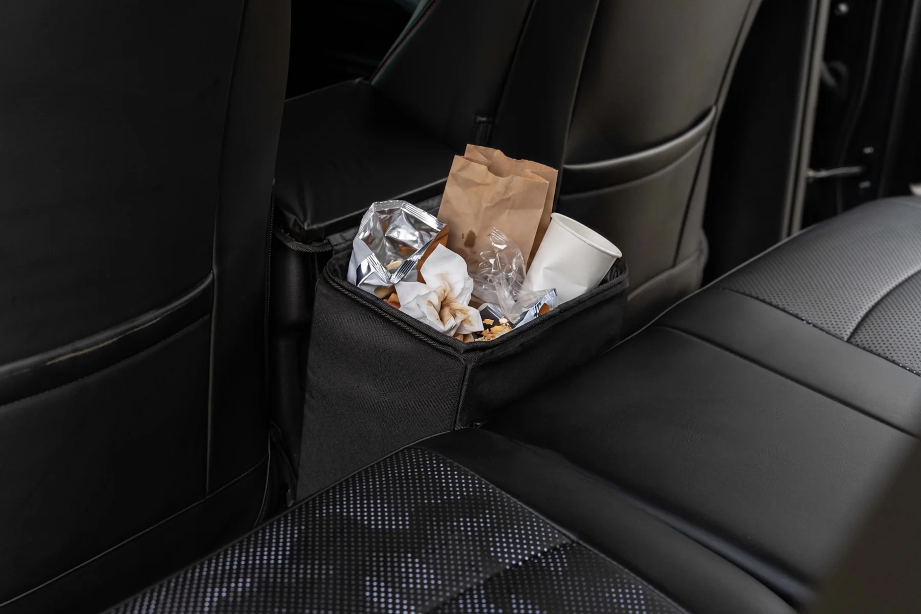 Open Double Deez Goodz car trash can holding food wrappers, napkins, a paper cup and snack packaging.